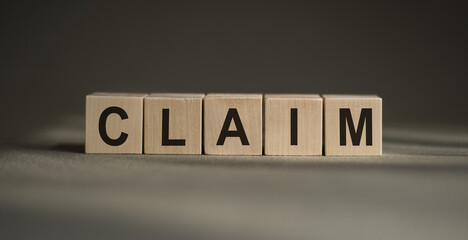 A wooden blocks with the word CLAIM written on it on a gray background.