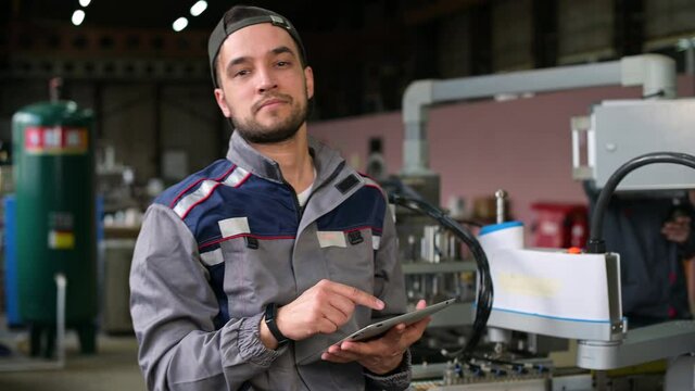 A young worker in a battery factory monitors the process and is distracted by the camera with a smile