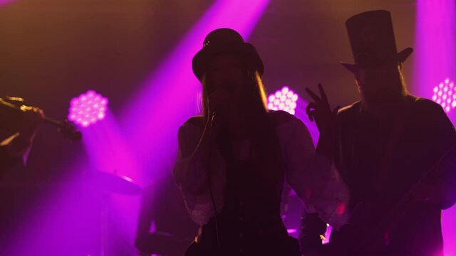 Dynamic performance of a rock band with a young female soloist in a dark smoky studio with purple lights. The band performs in Irish style clothing. Silhouette. Close up.