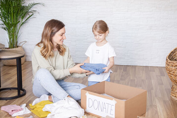 Happy family mother and daughter watched their clothes and put them in a paper box to donate. The...