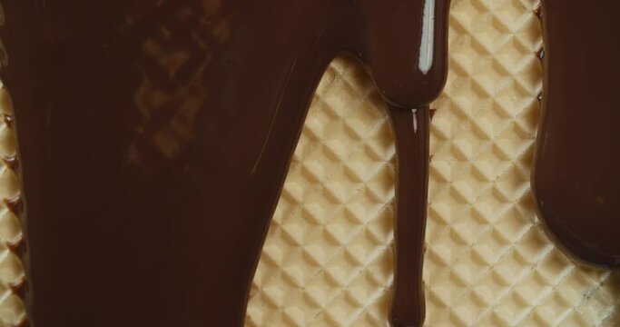 Close-up macro shot hot melted liquid chocolate flows over wafer surface, flowing molten dark chocolate stream. Cooking handmade wafer biscuits dessert. Confectionery. Pouring chocolate waves