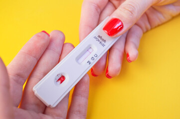 test for coronavirus on an orange background. medical analysis. a girl with a bright red manicure holds a test for antibodies to coronavirus, the result for antibodies is negative