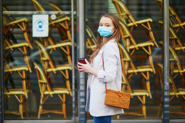 Young girl standing near closed restaurant in Paris and wearing protective face mask during coronavirus outbreak