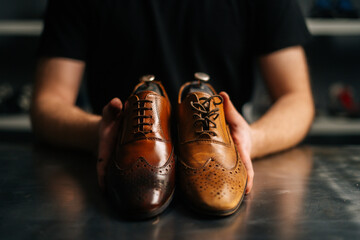 Close-up hands of male shoemaker holds old light brown leather shoe and repaired shiny shoes after...