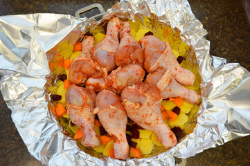 marinated chicken legs and chopped vegetables are placed in a mold and prepared for roasting
