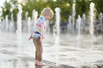 Little boy plays in the square between the water jets in the dry fountain at sunny summer day.