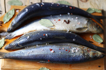 Salted herring of spicy salting. Spices and salt. Herrings with head and tail on a wooden board.