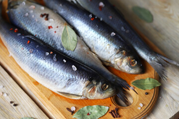 Salted herring of spicy salting. Spices and salt. Herrings with head and tail on a wooden board.