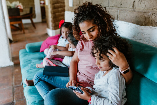 Latin Mother On Sofa At Home With Little Boy Child Use Phone Browse Internet Together In Mexico City