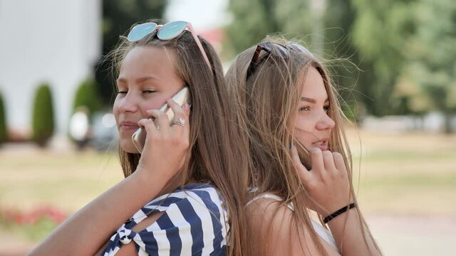 Two young girls talking on the phone on a summer day.
