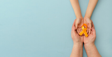 Hands of mother and child hold orange ribbon on blue background.Concept. World Multiple Sclerosis...