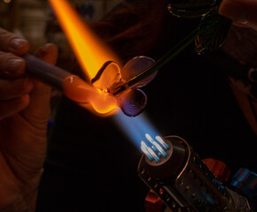 Hands of a glass artist, glass blower and their gas burner while making a decorative glass figure. Copy space