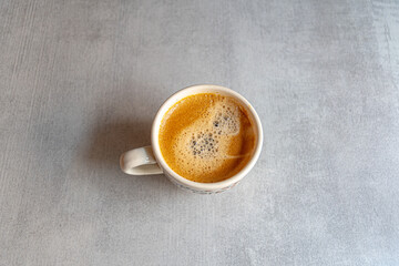 A cup of coffee in the morning light with an appetizing froth on a ceramic gray surface.