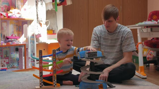 Man and boy playing cars on the floor childrens room