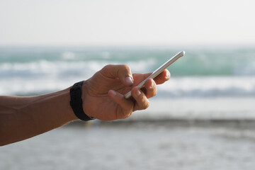 Close-up. Male hand with smartwatch using smartphone on the surf beach.