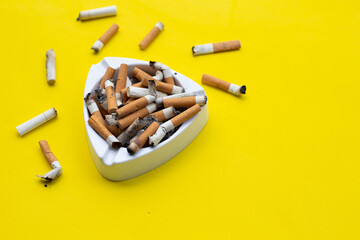 Ashtray and cigarettes on yellow background.