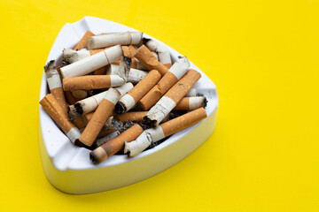 Ashtray and cigarettes on yellow background.