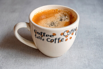 A cup of coffee in the morning light with an appetizing froth on a ceramic gray surface.