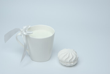 White cup of milk with a bow and marshmallows on a white background