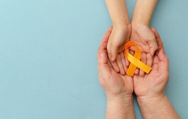 Hands of mother and child hold orange ribbon on blue background.Concept. World Multiple Sclerosis...