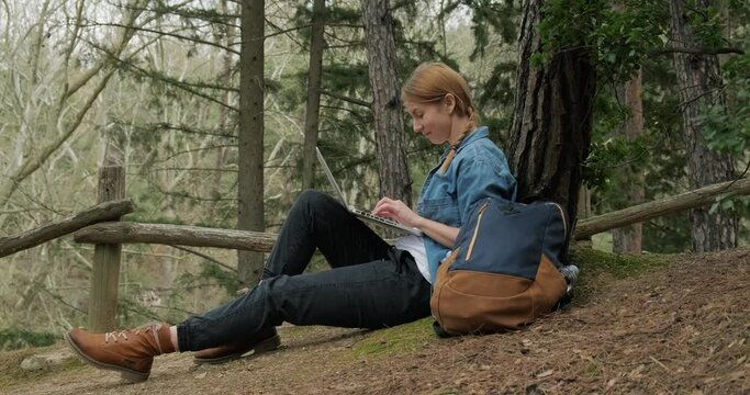 Freelancer woman using laptop in forest during hiking and traveling. Working remotely in nature. Fast 5g internet connection in forest.