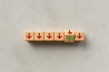 Line of down pointing red arrows on wooden cubes with one green arrow pointing up in a concept of...