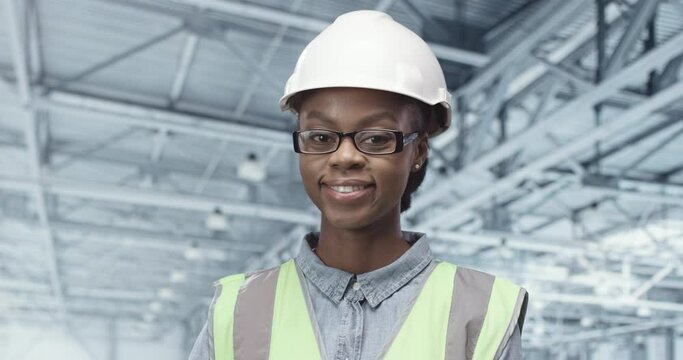 Close up portrait of cheerful beautiful young African American woman factory operator in glasses looking at camera and smiling standing at workplace. Female inspector with smile on face