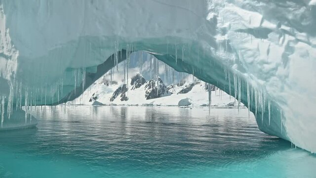 Closeup iceberg arch at turquoise ocean bay with mountains on snow aerial. Environment preserve