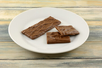 Candy bar of almond caramel covered in rich milk chocolate and pieces on white snack plate