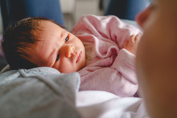 Close up portrait of newborn cute caucasian baby girl or boy looking to her mother - affection bonding and care concept