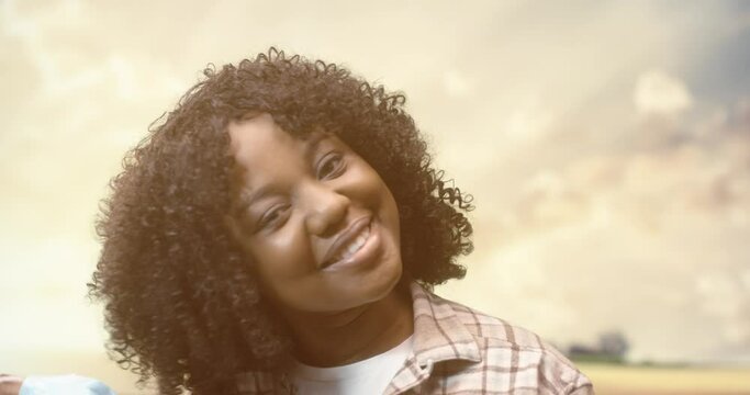 Cheerful young pretty African American female in positive mood standing outdoor in field in countryside, looking at camera and smiling removing medical mask from face. Young woman in village. Close up