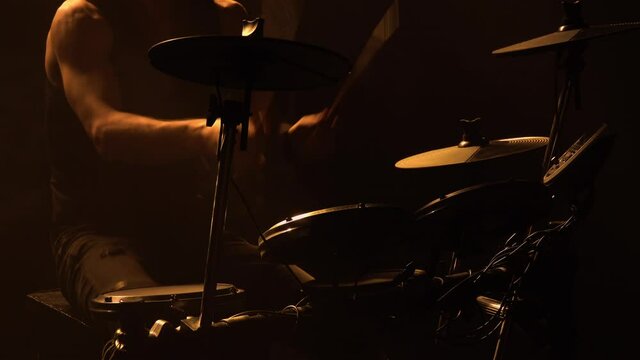 Professional musician playing drums and percussion cymbals in a dark smoky studio with yellow lights. Close up of the drummer torso pounds on the drum kit. Rock concert, live performance. Silhouette.