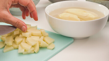 Chopping potatoes on chopping board close up on white kitchen table