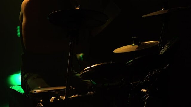 Professional musician playing drums and percussion cymbals in a dark smoky studio with yellow lights. Close up of the drummer torso pounds on the drum kit. Rock concert, live performance. Silhouette.
