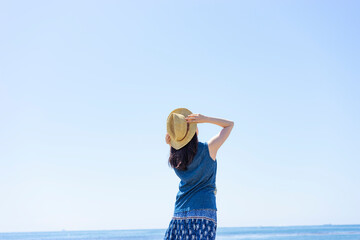 麦わら帽子を被った女性の後ろ姿と青空と海