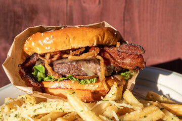 A freshly cooked, juicy western BBQ burger with cheese, fried, onions, lettuce, bacon, barbecue sauce on a sesame seed bun on a plate piled with garlic french fries.