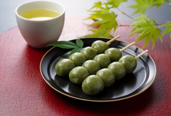 Grass dumplings and green tea placed on a red Japanese tray