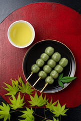 Grass dumplings and green tea placed on a red Japanese tray