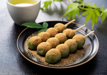 Grass dumplings covered with soybean flour and green tea served on a black plate set against a black background.