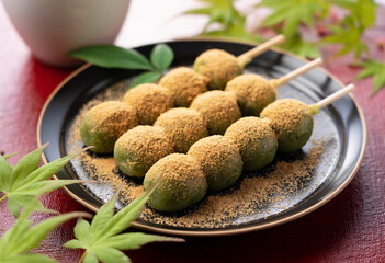 mugwort-flavored rice dumpling covered with soybean flour and green tea served on a black plate placed on a red tray.