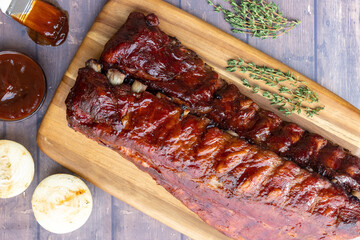 Overhead image of racks of smoked pork BBQ ribs on a board with fresh rosemary and grilled onions.