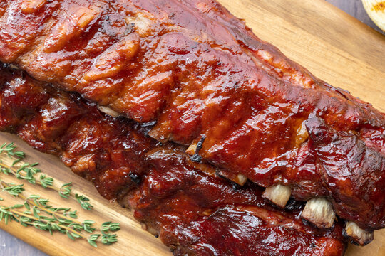 Overhead image of two racks of smoked pork BBQ ribs covered in BBQ sauce on a board with fresh rosemary