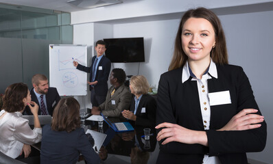Portrait of confident positive young business woman in meeting room with working group behind