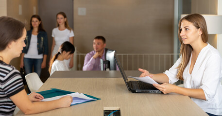Young female employee of staffing agency consulting clients at meeting in informal office interior