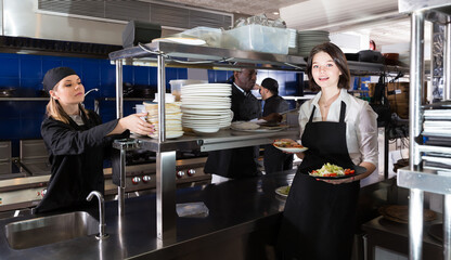 Portrait of glad waiter who is standing with order on kitchen in restaurant