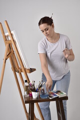 Close up  portrait of a red haired artist girl wearing casual clothes.  standing pose 
painting a canvas on an easel, against a studio background.