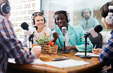 Positive male and female radio presenters talking with guest in studio