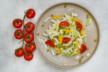 fresh summer vegetable salad with peking cabbage, cherry tomatoes, green peas and yellow bell pepper on a ceramic plate