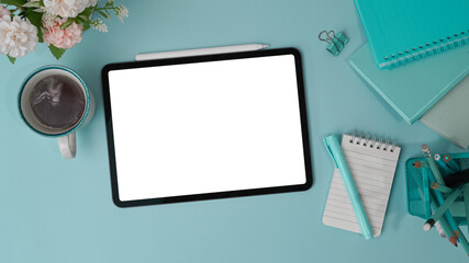 Top view of digital tablet with blank screen and various blue supplies on pastel blue background.