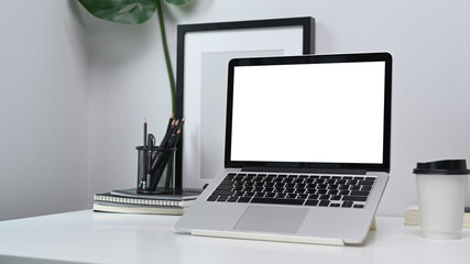 Fototapeta premium Mock up computer laptop with blank screen, pencil holder, coffee cup, notebook and empty photo frame on modern workplace.